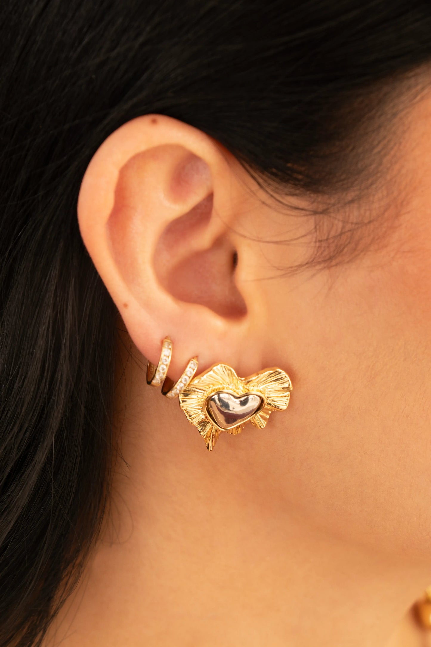 Aretes bicolor con corazón plateado y borde dorado ondulado en baño de oro 24K, fotografía en oreja de modelo.