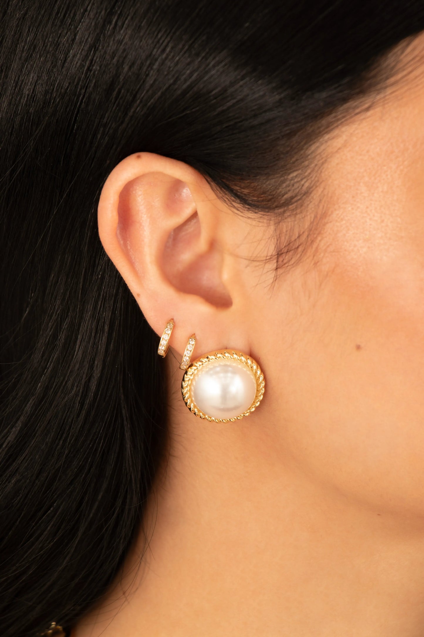 Aretes con perla grande y borde dorado trenzado en baño de oro 24K, fotografía de detalle en modelo.