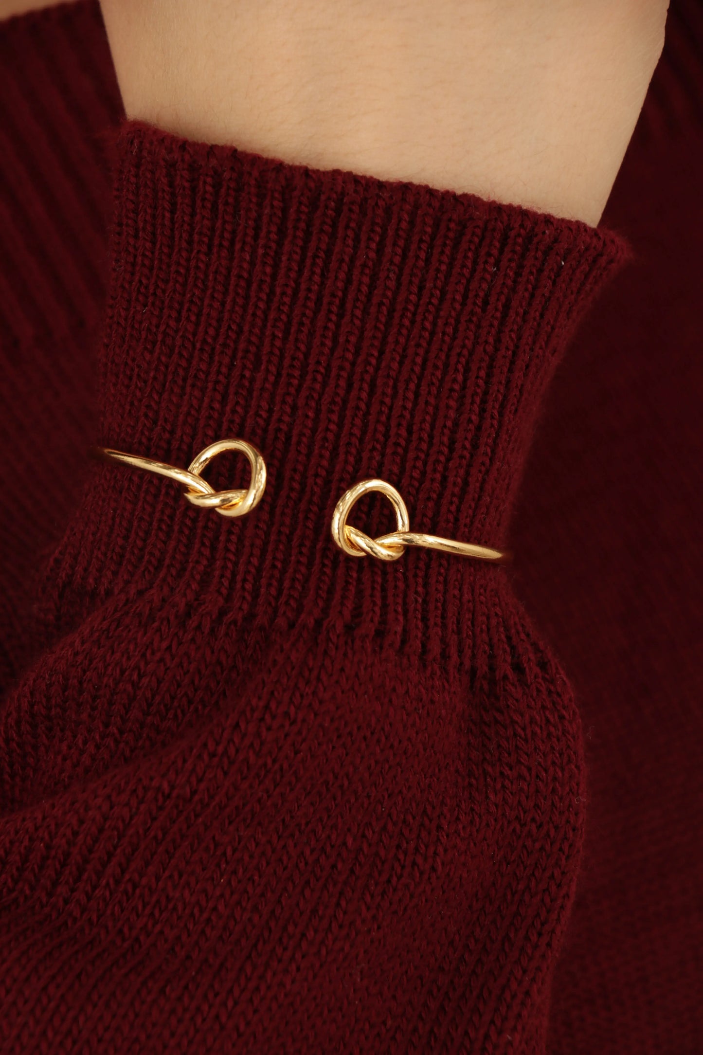 Brazalete tipo lazo en baño de oro 24K sobre fondo blanco, diseño delicado y ajustable con brillo pulido.