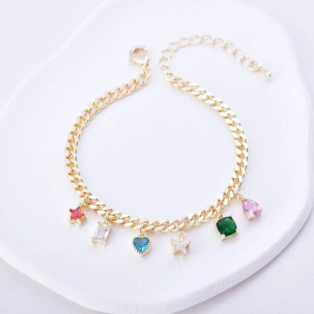 Pulsera dorada estilo eslabón con charms de colores en diferentes formas, en baño de oro 24K, sobre superficie blanca.