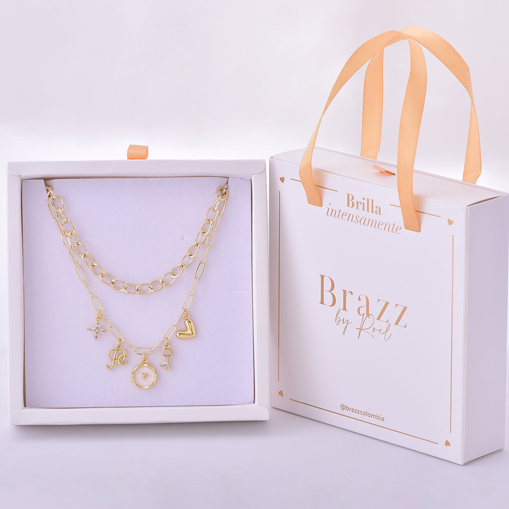 Set de collares dorados con dijes románticos como cruz, letra J, corazón, llave y charm circular, en caja Brazz by Roel.