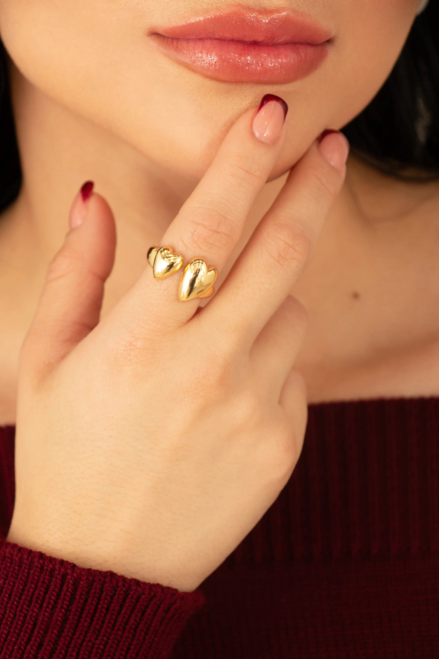 Anillo dorado ajustable con dos corazones brillantes en baño de oro 24K, fotografía en mano de modelo.