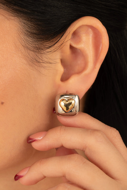 Arete bicolor con corazón en relieve dorado, fotografía de detalle sobre oreja femenina.