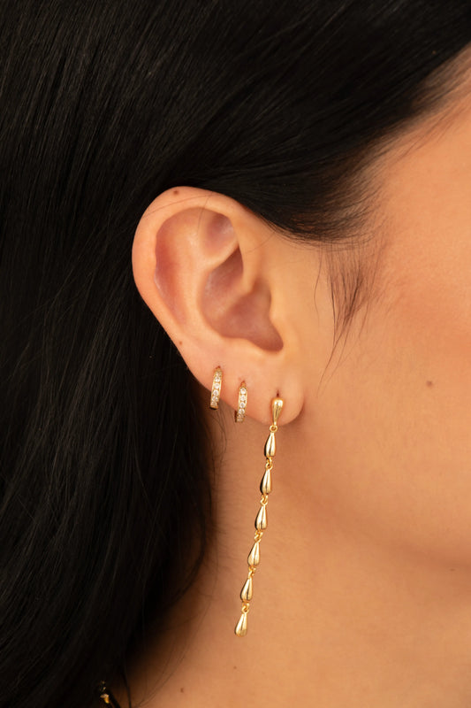 Aretes largos dorados con gotas articuladas en baño de oro 24K, fotografía en oreja de modelo.