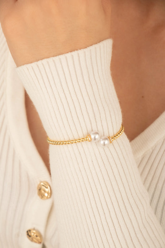 Brazalete dorado con dos perlas blancas en los extremos, fotografía en muñeca de modelo.