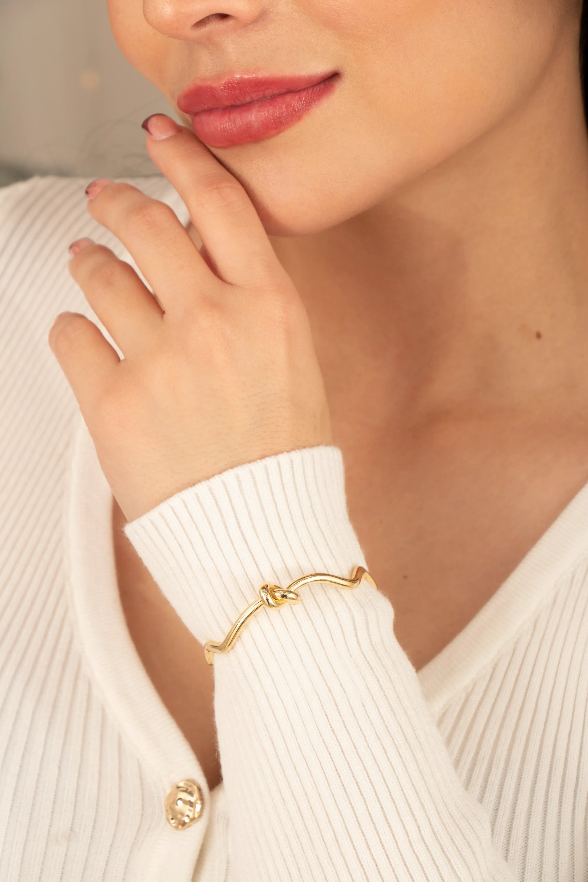 Brazalete dorado con nudo central en muñeca femenina, accesorio minimalista y moderno.