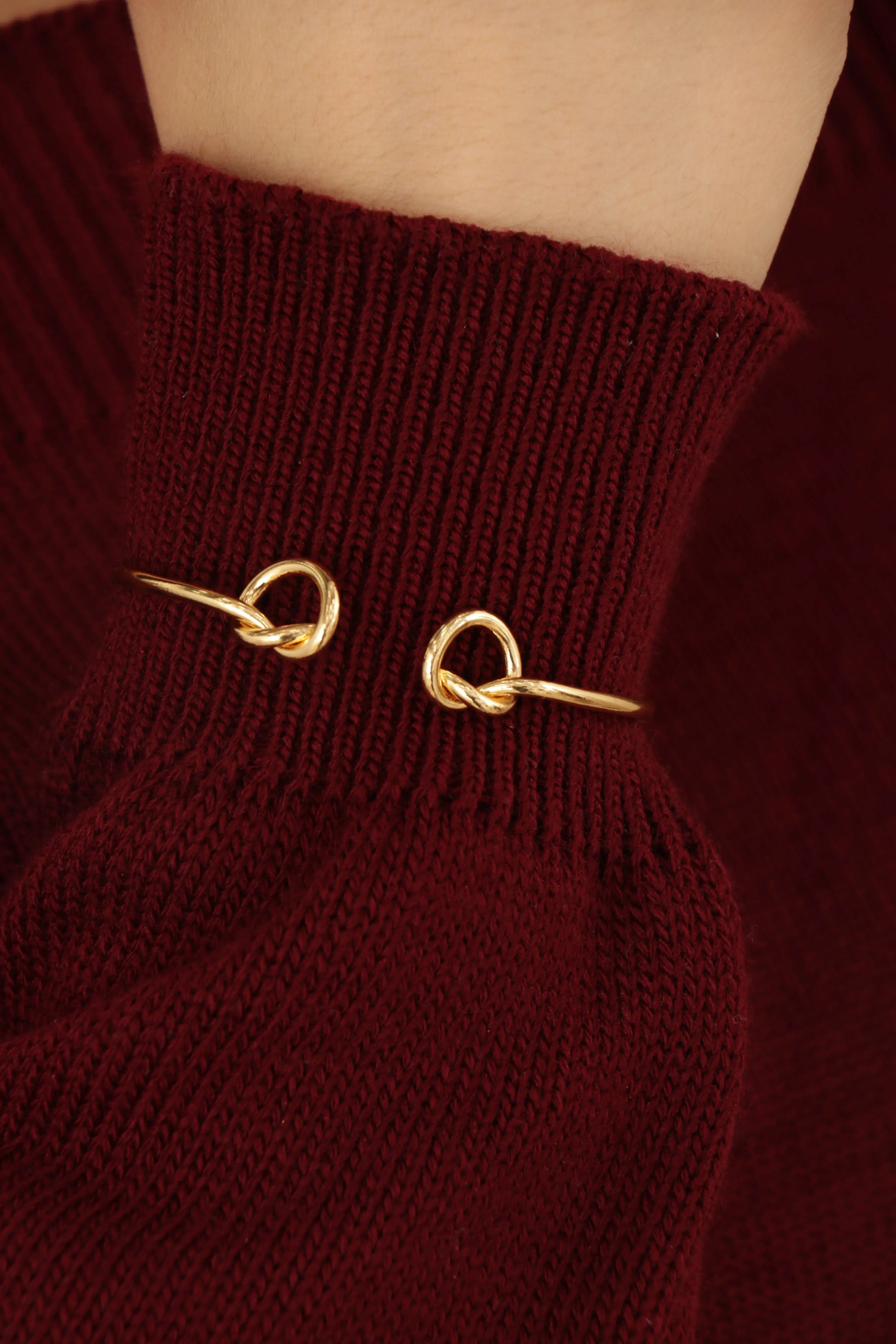 Brazalete tipo lazo en baño de oro 24K sobre fondo blanco, diseño delicado y ajustable con brillo pulido.