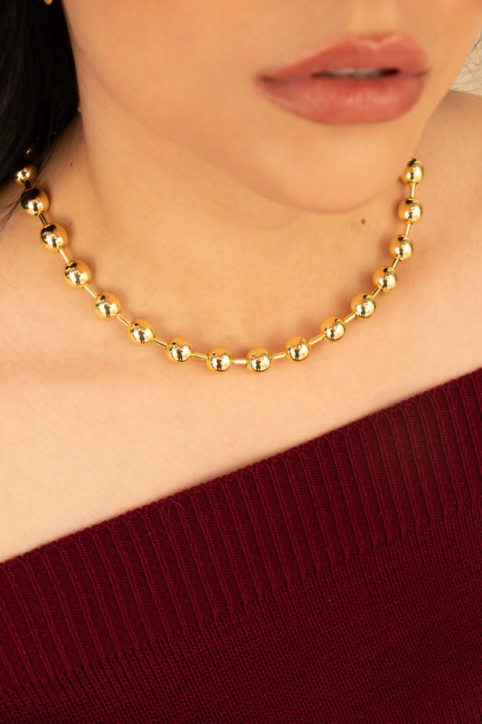 Collar de esferas doradas en baño de oro 24K, fotografía en el cuello de una modelo.