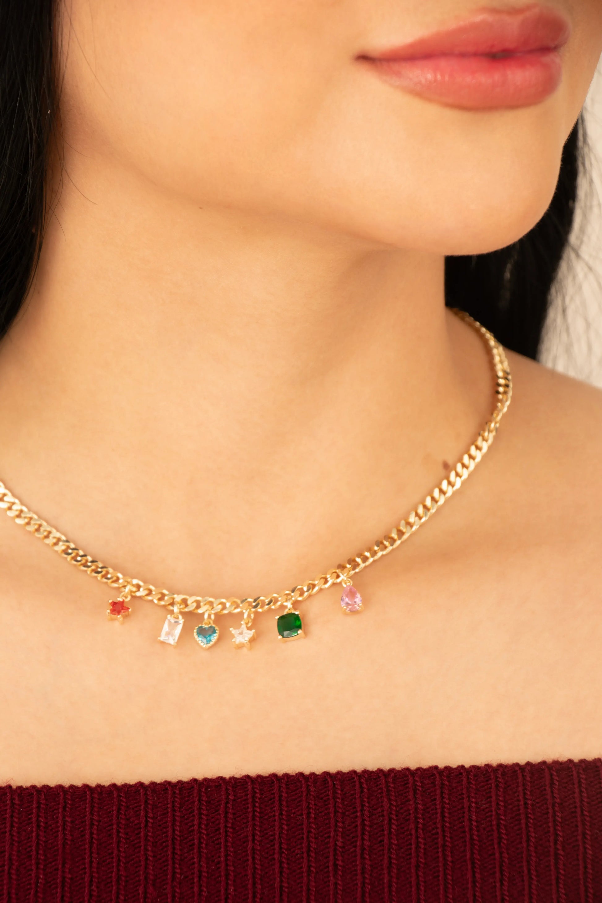 Collar dorado con charms de colores en forma de piedras y figuras, estilo eslabón, en baño de oro 24K, mostrado sobre el cuello de una mujer.