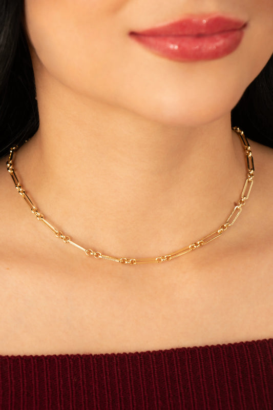 Collar dorado de cadena fina con nudos decorativos en baño de oro 24K, fotografiado en cuello de modelo.