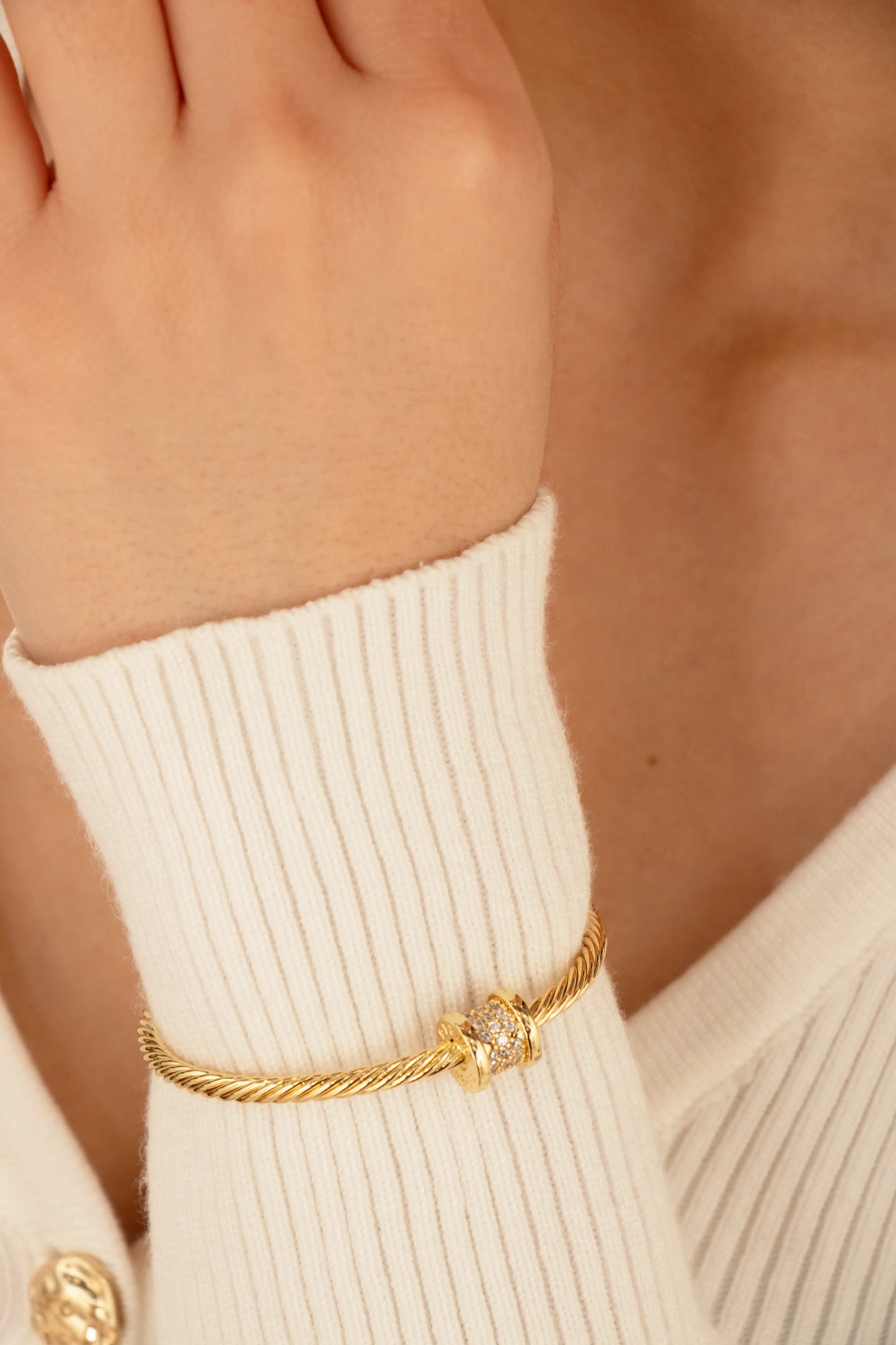 Pulsera dorada estilo cable con cilindro brillante, fotografía en muñeca de modelo.