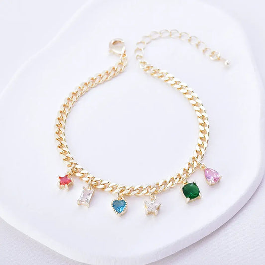 Pulsera dorada estilo eslabón con charms de colores en diferentes formas, en baño de oro 24K, sobre superficie blanca.