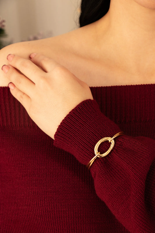 Pulsera rígida dorada con argolla ovalada en baño de oro 24K, fotografía en muñeca de modelo.