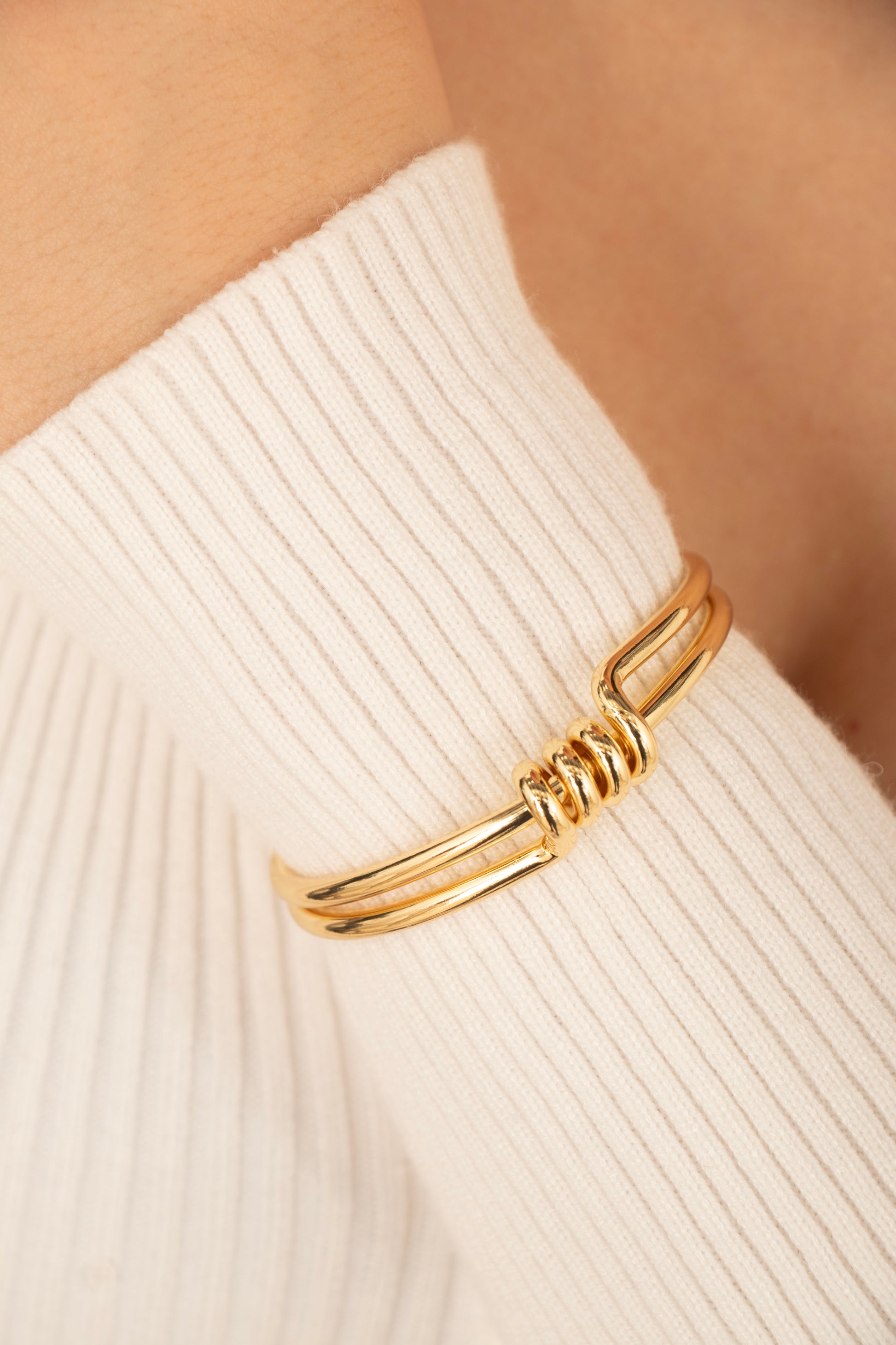 Pulsera rígida dorada con espiral central en baño de oro 24K, fotografía en muñeca de modelo.