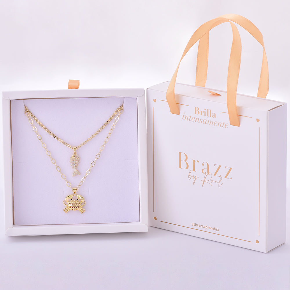 Set de collares dorados con charm de pez articulado y cangrejo, presentado en caja Brazz by Roel.